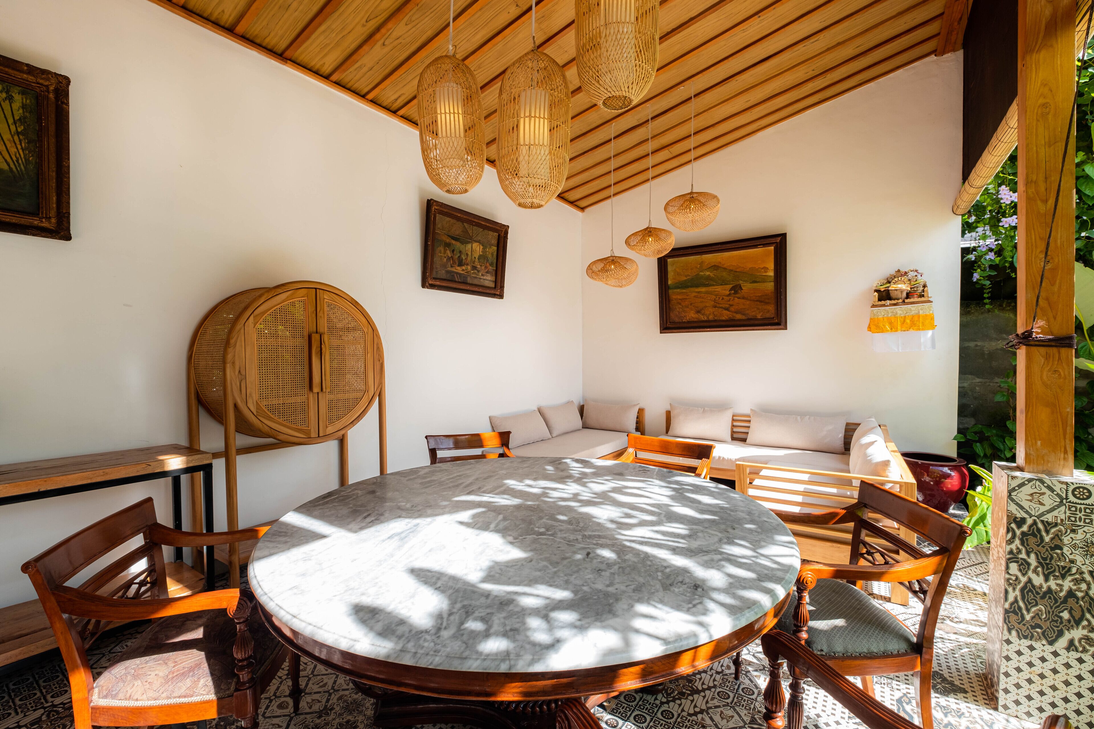 A round table with chairs, a wooden ceiling, and hanging wicker lights.