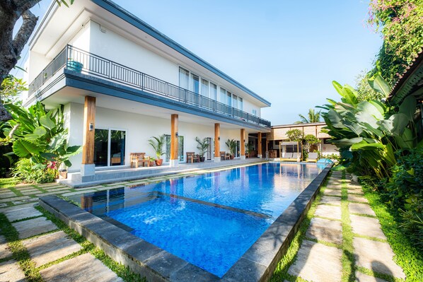 A modern two-story house with a swimming pool, large windows, and a balcony.