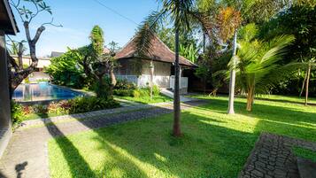 A well-maintained garden with a swimming pool, a thatched-roof structure, and a paved walkway.