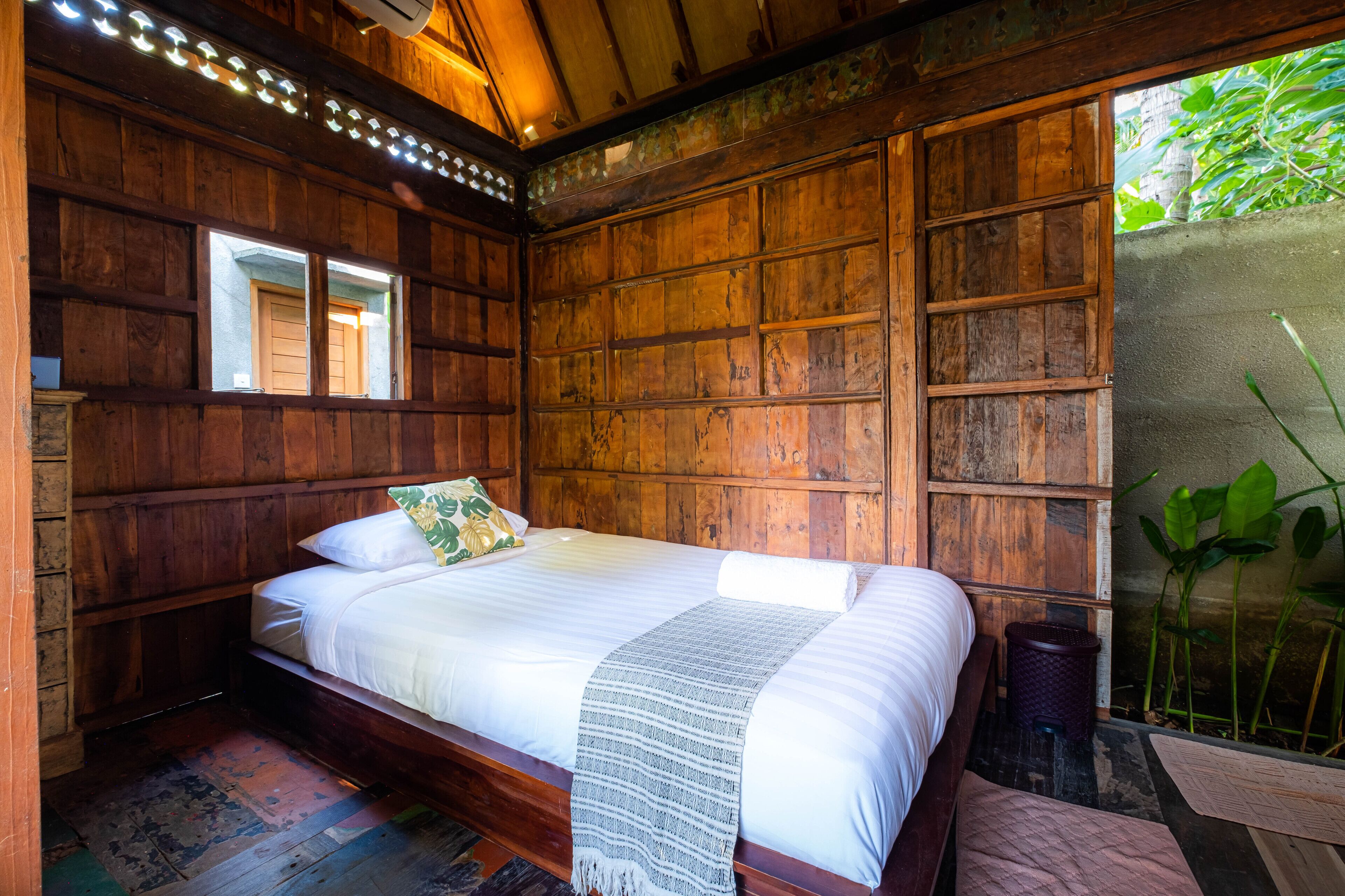 A wooden room with a bed, a window, and a view of greenery outside.