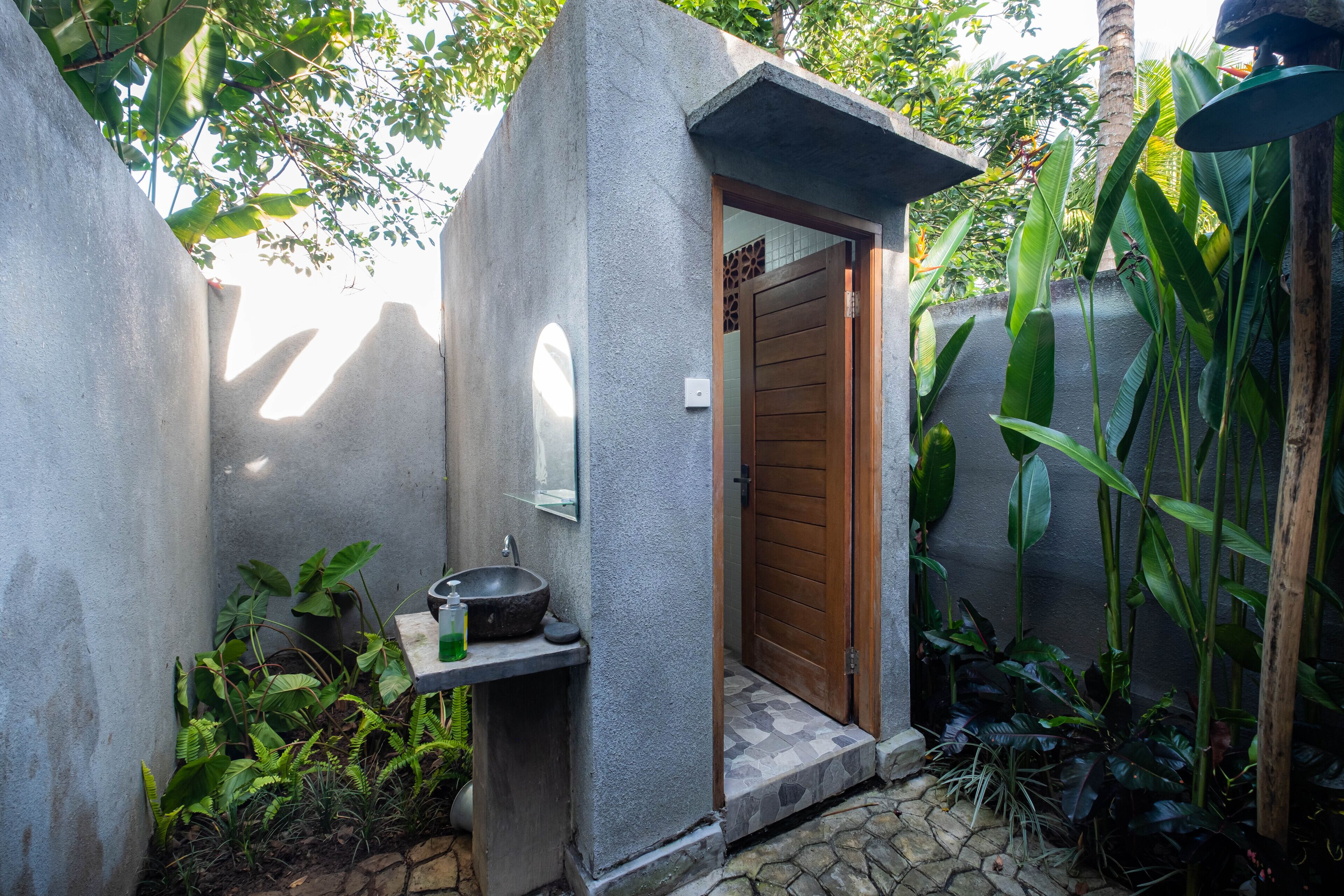 A small, private bathroom with a stone sink, a wooden door, and a small window.