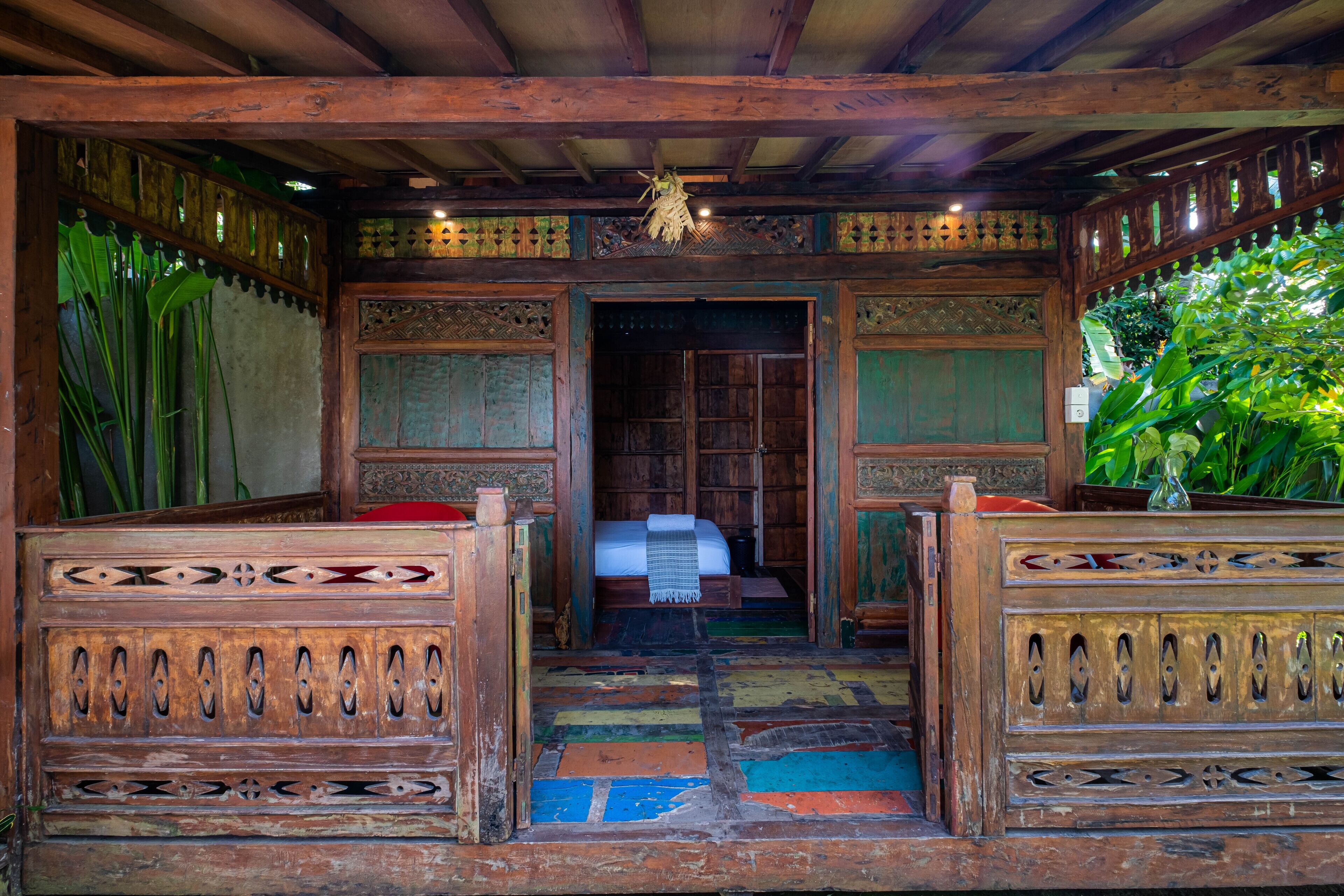 A traditional wooden room with a bed, a bench, and a door leading to another room.
