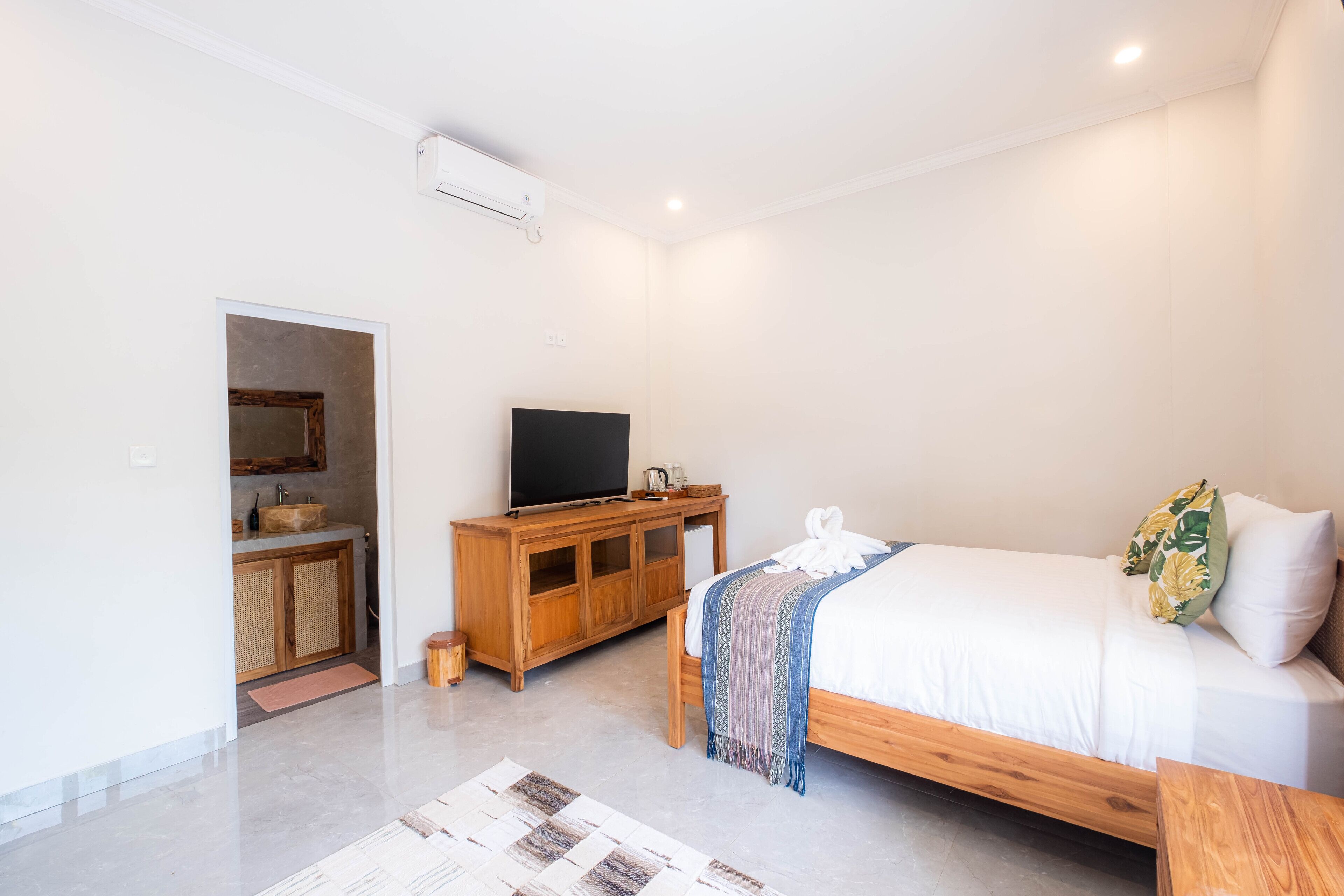 A bedroom with a bed, a wooden cabinet, a television, and a bathroom visible through an open door.