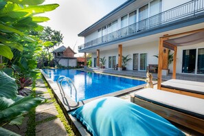 A modern pool area with a clear blue pool, a wooden deck, and a covered seating area.