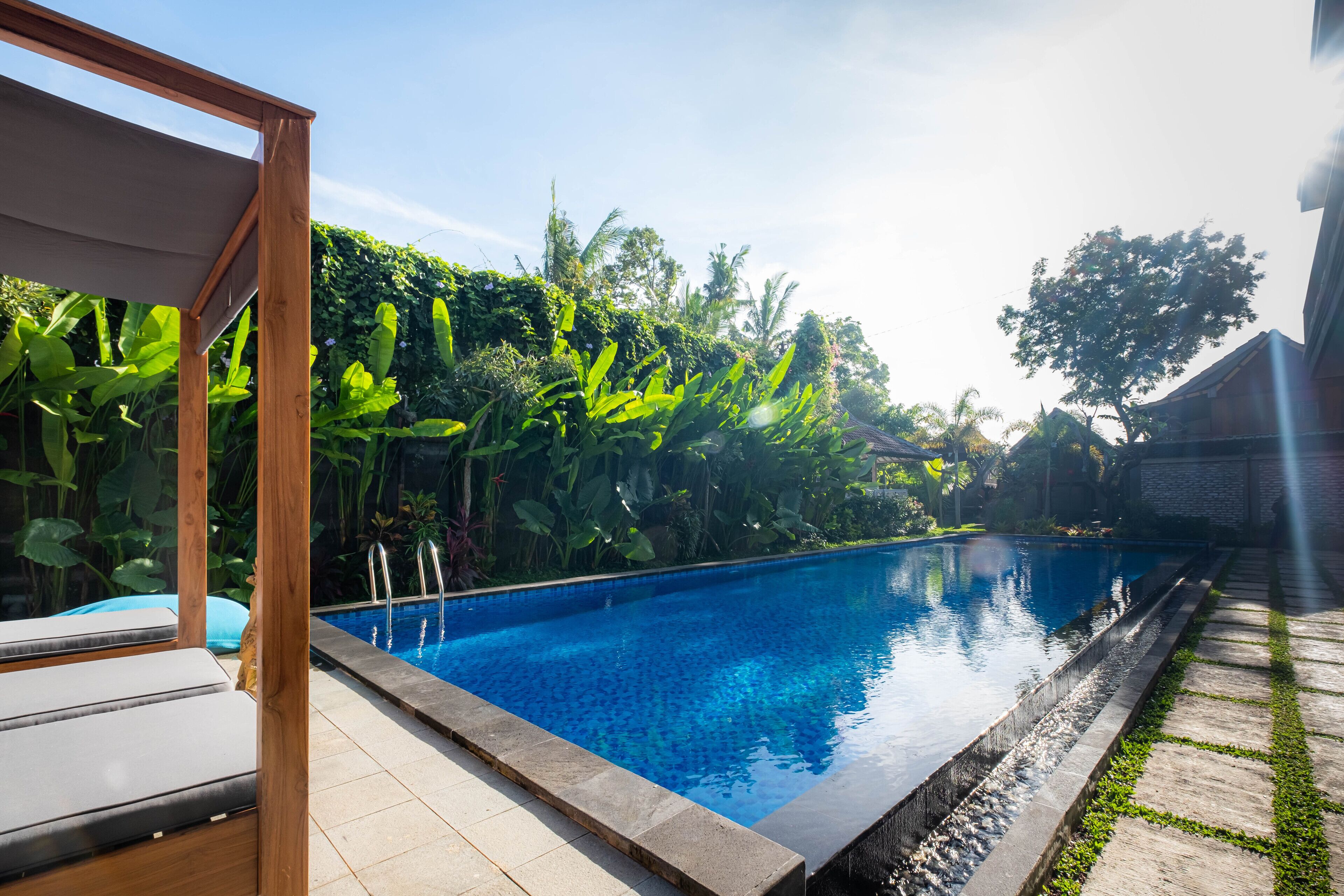 A swimming pool with a wooden deck and lounge chairs, surrounded by lush greenery.