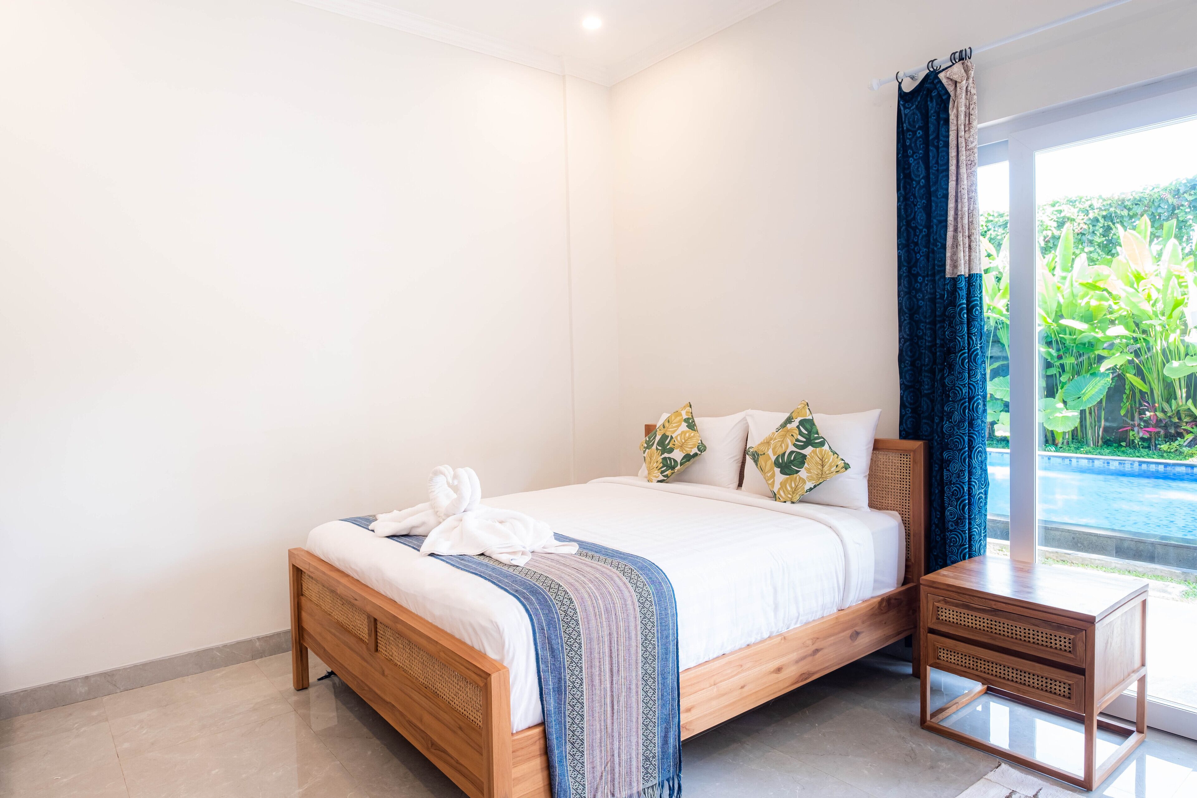 A bedroom with a wooden bed, a bedside table, and a view of a swimming pool.