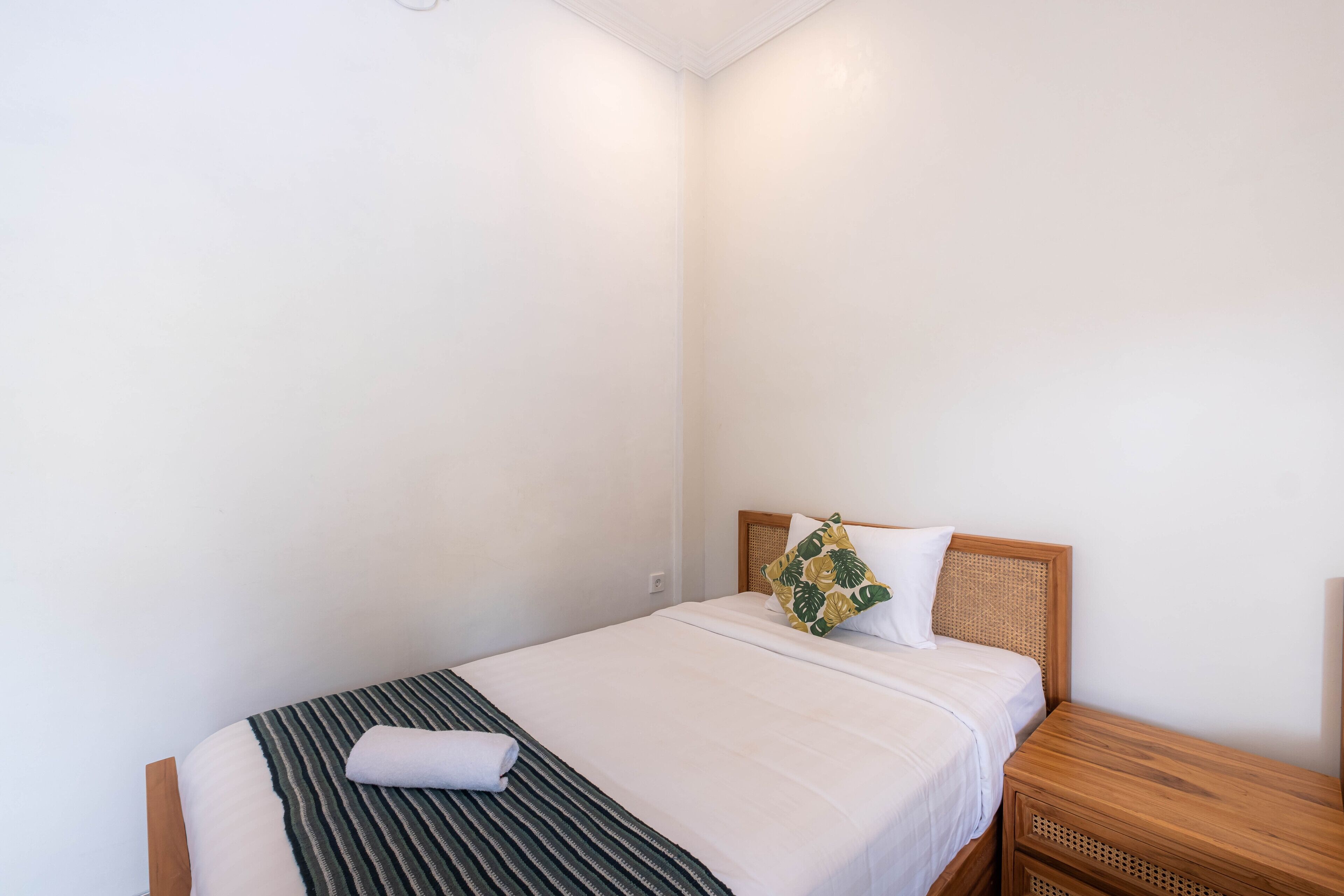 Un lit simple avec une couverture à rayures, un oreiller blanc et un autre oreiller assorti, orné d’un motif de feuilles.
