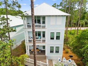 A multi-story building with balconies, a deck, and a view of surrounding greenery.
