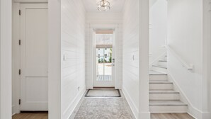 Un couloir étroit aux murs blancs et au plancher en bois, qui mène à un escalier et à une porte au fond.