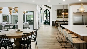 A modern kitchen with a central island, wooden flooring, and a dining area with a round table and chairs. - SWSS 6BR Luxury Group Retreat | Chef's Kitchen, Pool, Pickleball & Putting Green (Scottsdale)