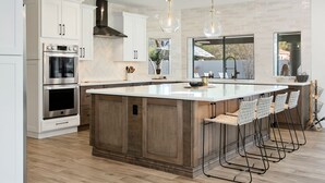 A modern kitchen with white cabinetry, stainless steel appliances, a large island with bar stools, and pendant lighting. - SWSS 6BR Luxury Group Retreat | Chef's Kitchen, Pool, Pickleball & Putting Green (Scottsdale)