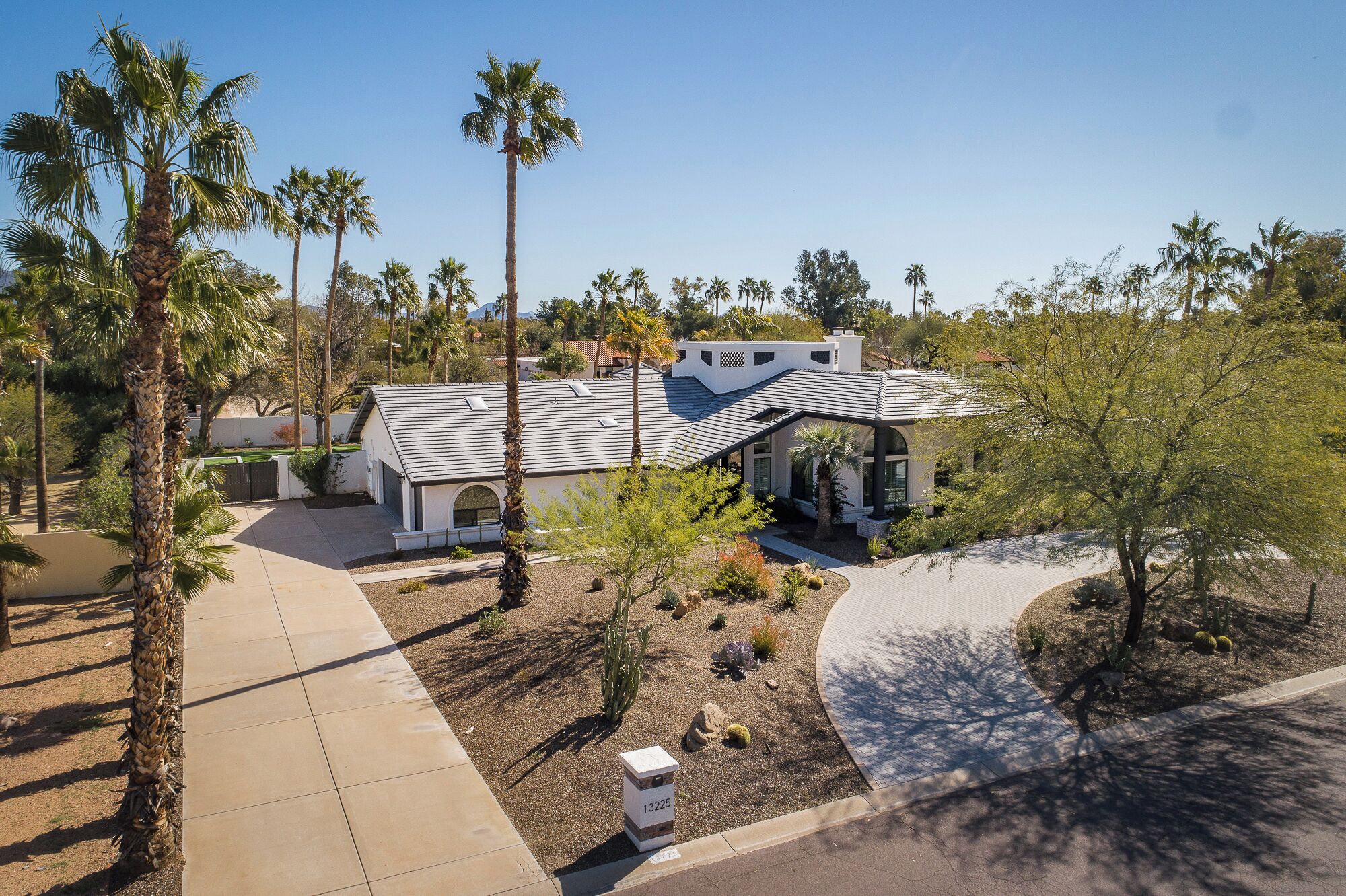 A modern house with a unique curved roof, surrounded by palm trees and a well-maintained garden.