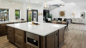 A spacious kitchen with a large island, dark wood cabinets, and a modern pendant light. - SWSS 6BR Luxury Group Retreat | Chef's Kitchen, Pool, Pickleball & Putting Green (Scottsdale)