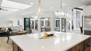 A spacious kitchen with a large island, modern pendant lights, and a sleek stainless steel refrigerator. - SWSS 6BR Luxury Group Retreat | Chef's Kitchen, Pool, Pickleball & Putting Green (Scottsdale)