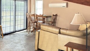 A cozy room with a wooden ceiling, a beige sofa, a dining table with chairs, and a window with curtains.