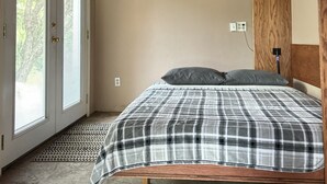A bedroom with a wooden ceiling, a bed with a plaid bedspread, and a door with frosted glass windows.