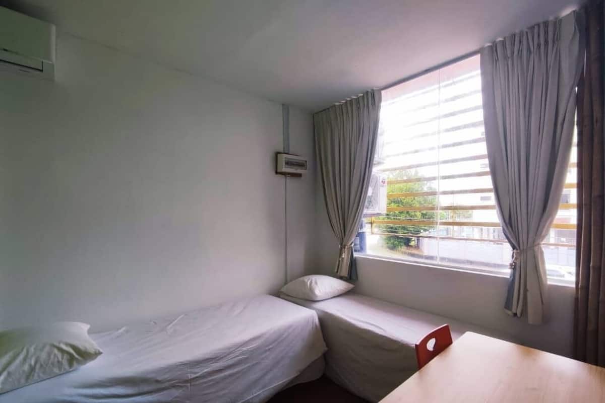 A small, single-room accommodation with a bed, a table, and a window with curtains.