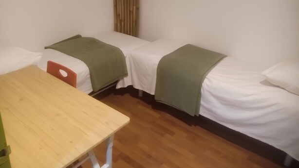 A room with two single beds, a wooden table, and a vertical bamboo curtain. - Natol Budget Homestay Rock Road (Kuching)