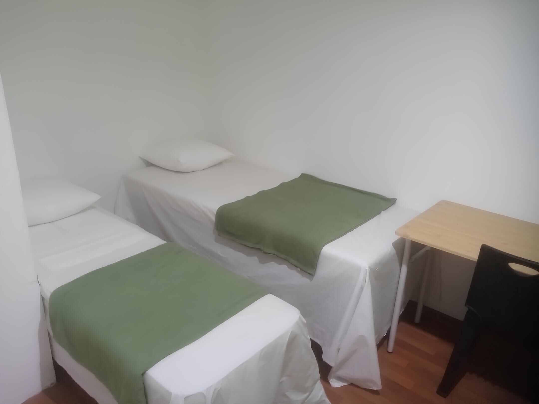 Een kleine, schone kamer met twee eenpersoonsbedden, een houten bureau en een stoel.