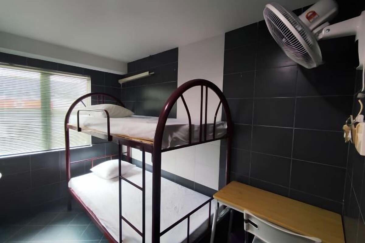 A bunk bed room with a ceiling fan, a small table, and a window with blinds.