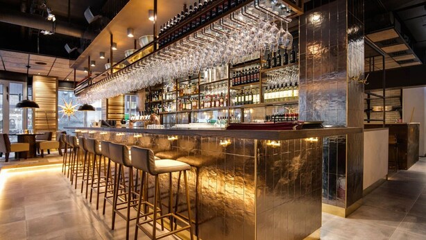 A modern bar area with a long counter, multiple stools, and a wine rack with bottles and glasses. - Stockholm City Chic-1-Bedroom Loft for 3 (Stockholm)