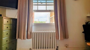 Een kamer met een raam, een radiator, een groene dressoir en een klok aan de muur.