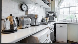 Een moderne keuken met witte apparaten, een klok en een raam met uitzicht op groen.
