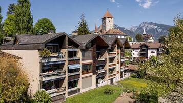 Un immeuble à plusieurs étages doté de balcons, d’une tour et ayant une chaîne de montagnes en arrière-plan.