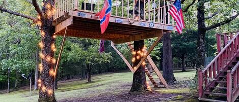 A wooden deck with two flags, surrounded by trees and a grassy area.