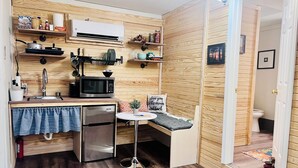 A compact kitchen with a microwave, sink, and refrigerator, wooden walls, and a small seating area with a sign.
