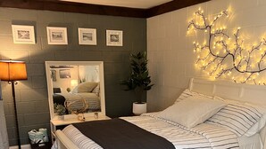 A bedroom with a bed, nightstands, a mirror, a lamp, and a wall-mounted light fixture.