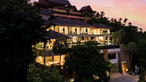 A multi-story resort with a pool, lush greenery, and a sunset sky.