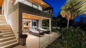 A modern house with a glass balcony, a pool, and a staircase.