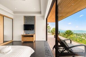 Un dormitorio moderno con una cama grande, un televisor instalado en una pared de piedra y un balcón con vistas al mar.