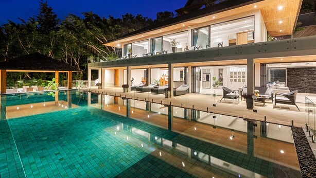 A modern resort with a large pool, outdoor seating, and a two-story building with glass walls.