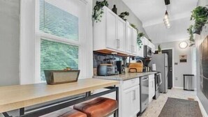 A modern kitchen with white cabinets, a wooden countertop, and two leather bar stools. - Serenity House | 2BR | 7 Min to Downtown ATL | Large Patio (Atlanta)