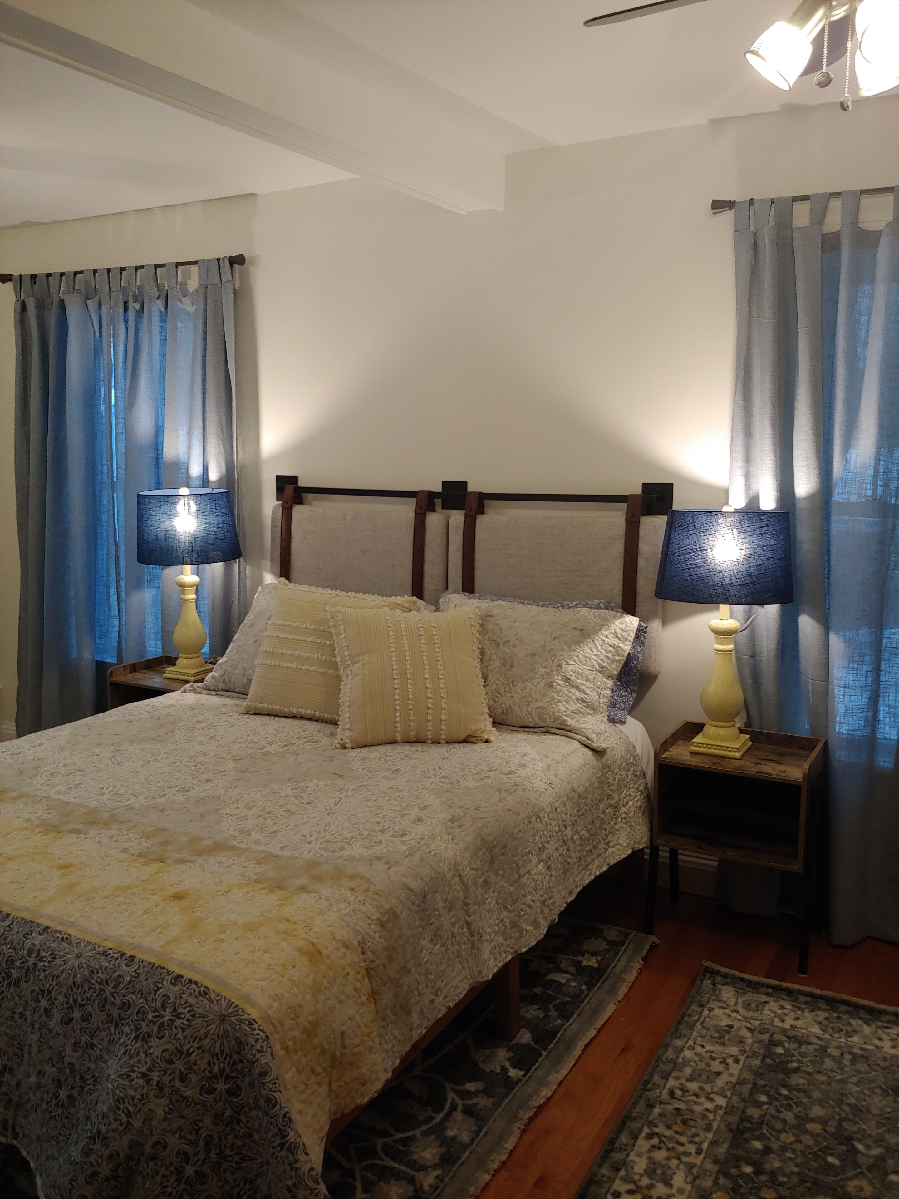 A bedroom with a bed, two bedside tables with lamps, a headboard, and curtains.