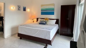 A bedroom with a bed, a ceiling fan, a painting, and a nightstand with a lamp.
