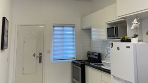 A modern kitchen with white cabinets, a black countertop, a stainless steel stove, a white refrigerator, and a ceiling light fixture.