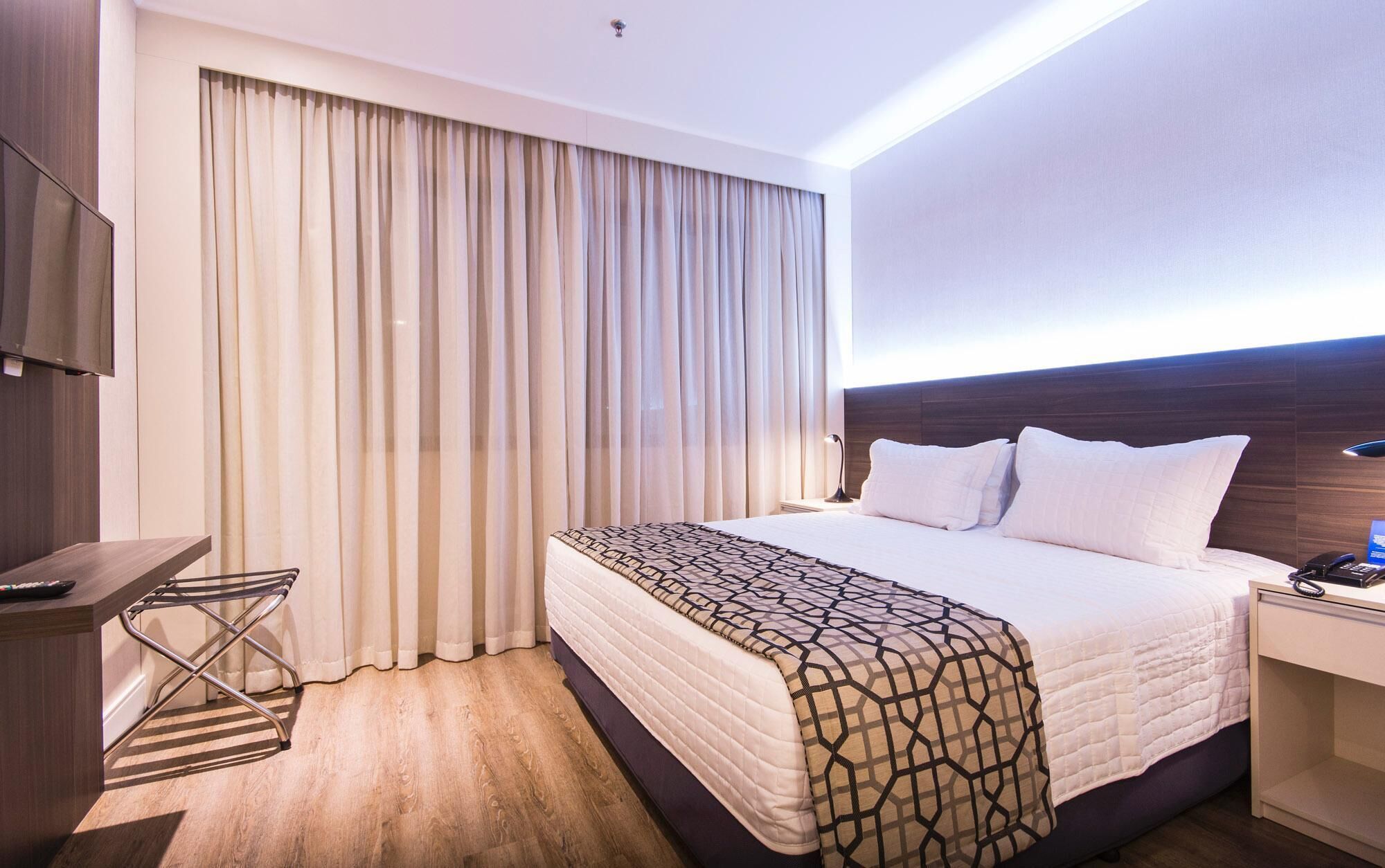 A hotel room with a bed, a desk, a chair, and a TV.