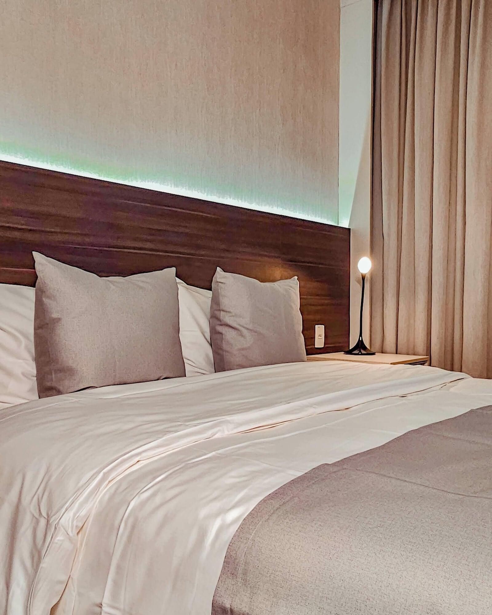Habitación de hotel con una cama grande, una mesita de noche, una lámpara y vistas al exterior.