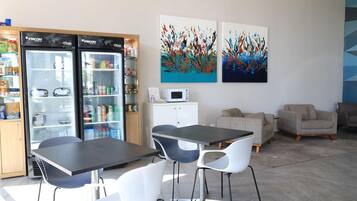 Una habitación moderna con una mesa negra, sillas blancas, un armario blanco y dos cuadros abstractos en la pared.