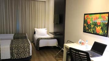 Habitación de hotel con dos camas, un escritorio con una computadora portátil, una silla, un televisor y un cuadro de flores.