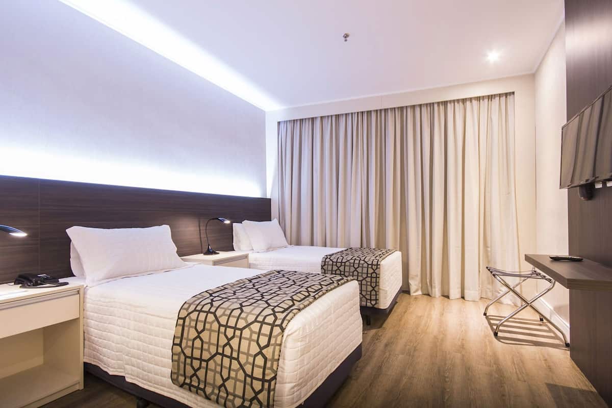 Une chambre d’hôtel avec deux lits, un bureau avec une lampe, une télévision et une fenêtre avec des rideaux.