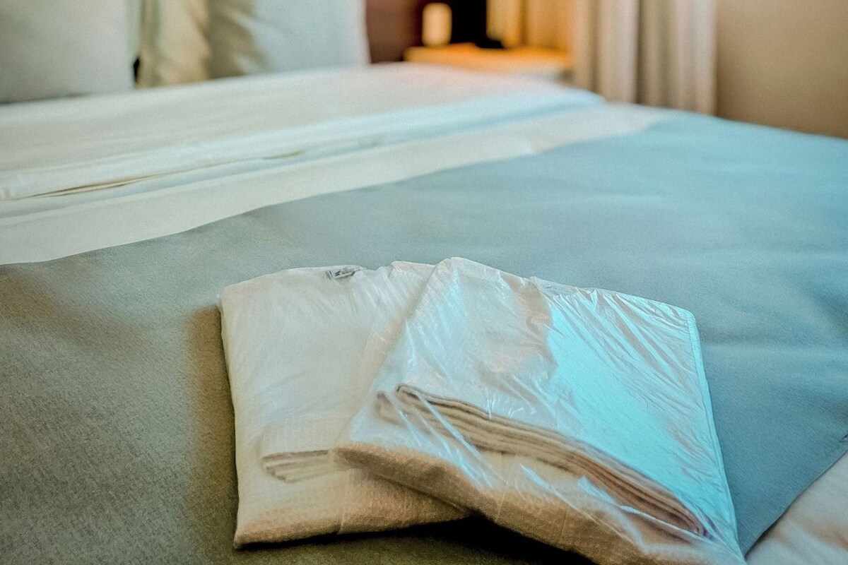 A hotel room with a neatly made bed, a nightstand with a lamp, and a window with curtains.