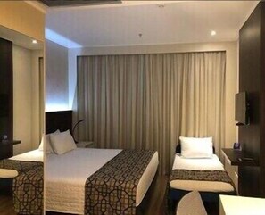 Habitación de hotel con dos camas, un ventanal con cortinas, un televisor de pantalla plana y una pared decorativa de piedra.
