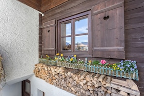 Un bâtiment rustique en bois, doté d’une fenêtre, d’une clôture en bois et d’une pile de bois de chauffage.