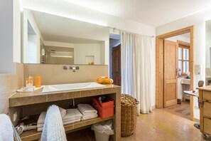 Ein Badezimmer mit großem Spiegel, Waschbecken und Dusche. Auf der Ablage liegen Handtücher und Toilettenartikel.