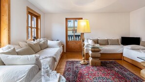 A room with a bed, a sofa, a television, and a wooden floor.