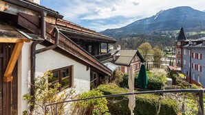 A traditional chalet with a balcony, a wooden facade, and a view of a mountain range.